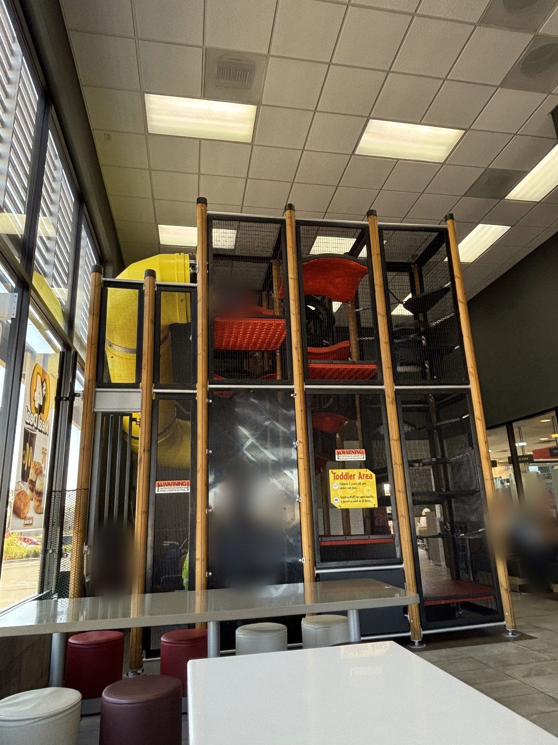 601 N Stephanie店のPlayPlace。黄色いチューブ滑り台と、赤い足場が縦に積まれた立体遊具。手前は席とスツール（撮影：YO-MIDOKORO、2026年7月30日。人物はぼかしています）